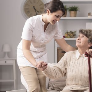 Young carer supporting senior disabled woman with walking stick.